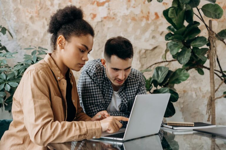 Two young adults collaborate on a project using a laptop in a modern workspace.